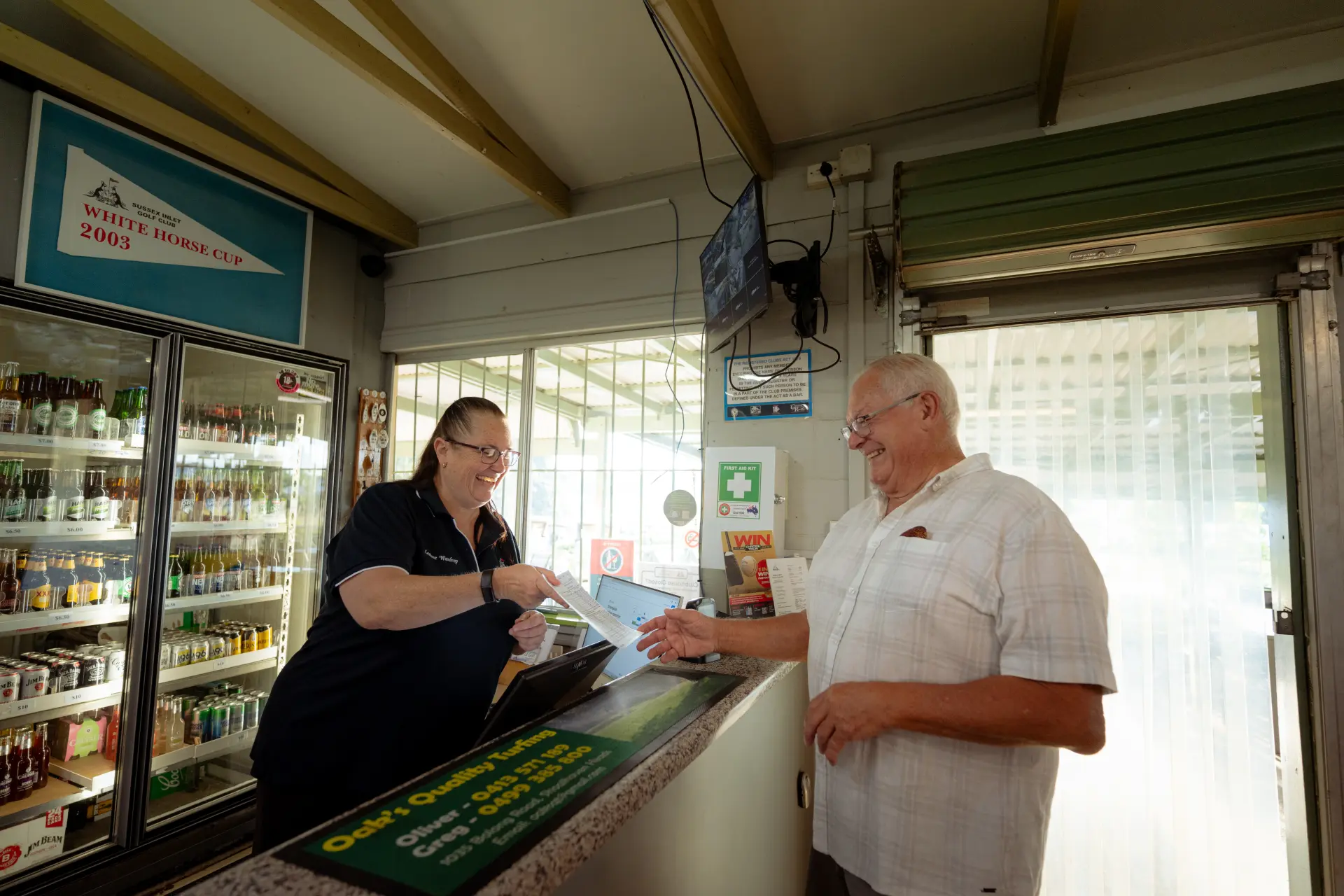A golfer and a staff member sharing a laugh over a scorecard at the pro shop counter